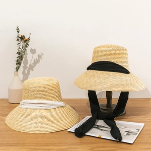 Flat top straw sun hats with black and white ribbon ties displayed on a wooden table
