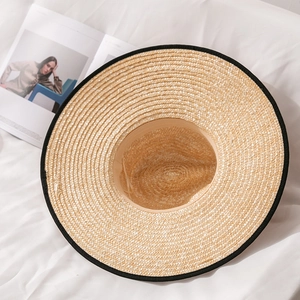 Detail of a wide brim straw hat with black grosgrain edging and dense woven texture