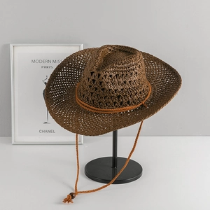 Detail of a dark brown western straw hat with hollow weave and a decorative wind cord
