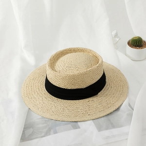 Detail of woven straw texture and wide black ribbon on a beige flat-top sun hat