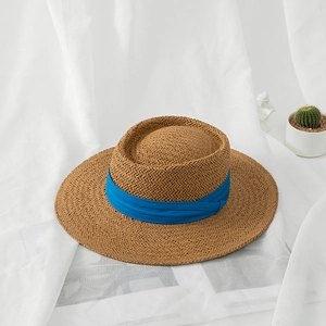 Detail of hand-woven straw hat with blue ribbon on a white textured background