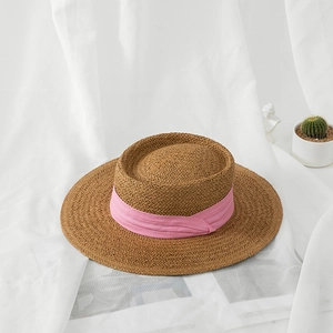 Detail of a brown woven straw hat with flat top and pink ribbon on white fabric