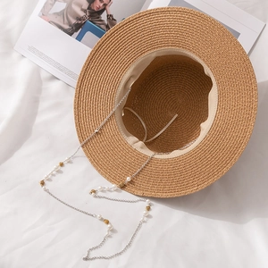 Chapeau de paille à sommet plat avec chaîne de perles élégante sur tissu blanc