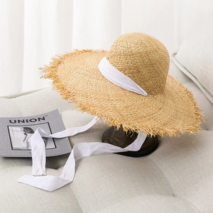 Wide brim raffia straw hat with fringe edges and white lace ribbon for beach holidays