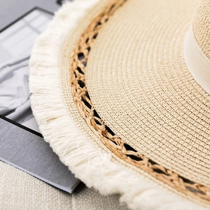 Detail of beige straw hat with woven texture, hollow band, and white fringe brim
