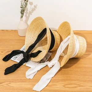 Detailed top view of natural straw hats with long chiffon ribbons on wooden texture