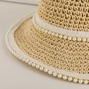 Dettaglio macro del cappello in paglia intrecciata beige con finiture in perle e nastro