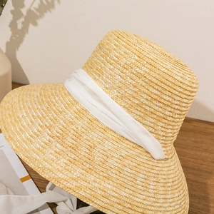 Detail of flat top straw sun hat featuring thick natural weave and white ribbon band