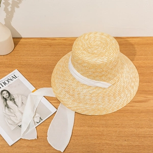 Detail of wide brim straw sun hat with elegant white chiffon bow ribbon on wood surface