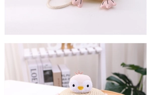 Detail of children's straw bag featuring a cute pink crown penguin plush on beige weaving