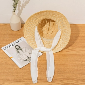 Detailed top view of a woven straw sun hat with white chiffon ribbon on a wooden desk