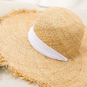Detail showing woven raffia texture with white ribbon and frayed edges on a sun hat