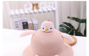 Detail of pink straw sun hat for children featuring a cute penguin doll and plush wings