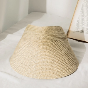 Detail of straw woven visor hat in light beige on a soft fabric background with a book