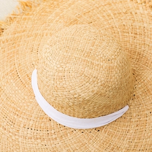 Detailed close-up of woven raffia sun hat with white ribbon and frayed tassel edges