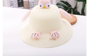 Detail of cute cream straw sun hat for kids with pink penguin plush features and soft wings