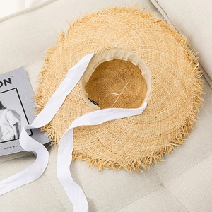Detail of raffia sun hat with frayed edges and white lace ribbon on a soft grey sofa