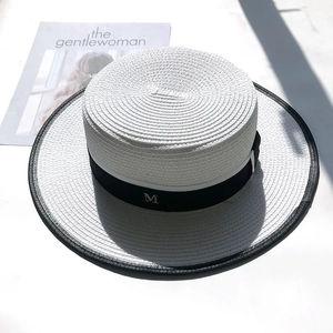 Detail of white boater hat with black ribbon, M-logo metal accent, and contrast binding