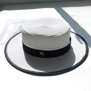 White boater straw hat with black trim and gold M letter metal accessory on the ribbon