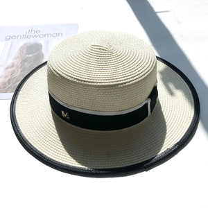 Detail of white straw boater hat featuring black ribbon with a golden M metal logo
