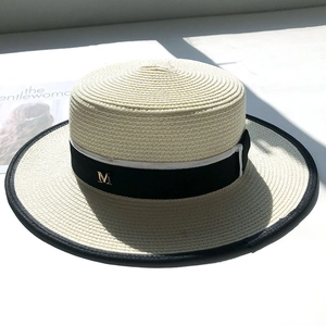 Chic cream boater straw hat with M letter logo and ribbon detail on a fashion magazine