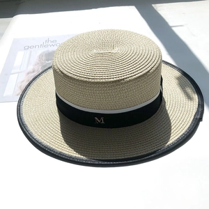 Detail of white boater hat with black trim, ribbon band and gold metal M logo