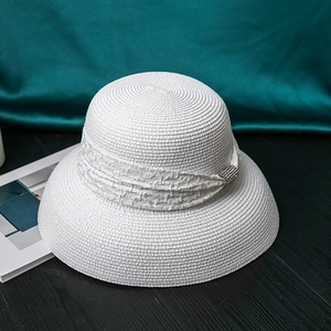 Detail of white straw hat featuring a silver rhinestone buckle on the ribbon trim