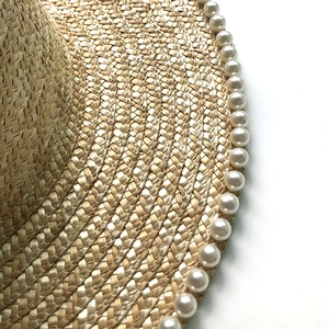 Detailed macro of fine wheat straw weave with white pearl embellishments on the brim