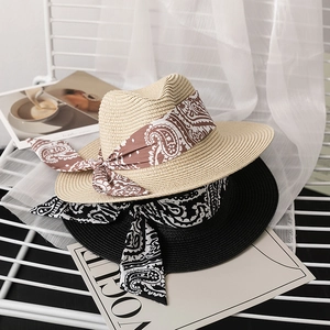 Beige and black straw sun hats with paisley ribbons on a stylish white mesh chair