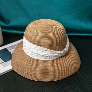 Close-up of brown straw hat with white pleated band and silver rhinestone buckle decoration