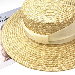 Vue détaillée du chapeau canotier en paille naturelle avec ruban crème et magazine