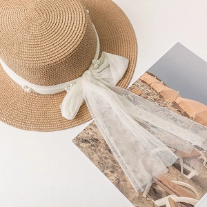 Detail of straw hat with white mesh bow and pearl embellishments on flat lay