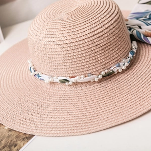 Détail du chapeau de paille rose avec ruban floral et accents de perles blanches