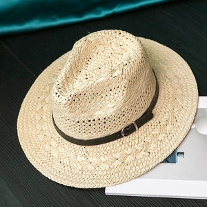 Detail of light beige straw hat with black faux leather band and silver buckle on wood
