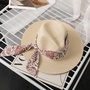 Detail of woven straw sun hat featuring a brown paisley ribbon bow on a mesh rack