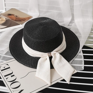 Flat top straw sun hat with black woven texture and rhinestone bow on a fashion set