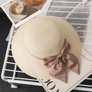 Detail of a beige straw hat with fine weave texture and a large brown satin ribbon bow