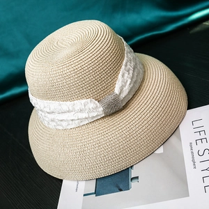 Close-up of beige straw hat with white fabric band and sparkling rhinestone buckle