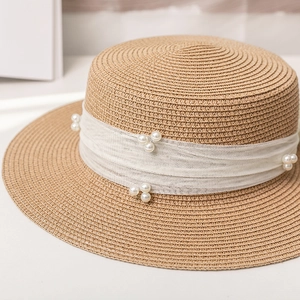 Close-up detail of flat top straw hat with white mesh ribbon and elegant pearl accents