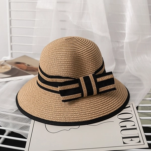 Detail of a straw sun hat featuring a striped bow and black trimmed edge on a chair