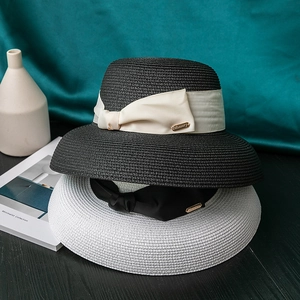 Elegant wide-brim straw hats in black and white with decorative bow ribbons and metal tags