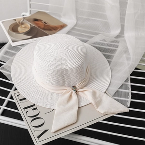 Detail of white straw sun hat with chiffon ribbon bow and gemstone decoration