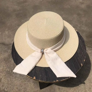 Flat top straw hat with wide brim and white ribbon featuring a rhinestone buckle