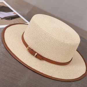 Détail d'un chapeau de paille beige à bord plat avec ruban en cuir brun et boucle dorée