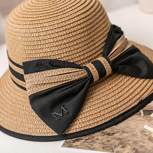 Détail d'un chapeau de paille tissé avec ruban noir, nœud et accent de lettre M en métal