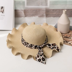 Straw sun hat with leopard ribbon bow and wide wavy brim for women on a desk
