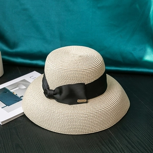 Detail of wide brim straw hat with elegant black ribbon bow and gold metal logo charm
