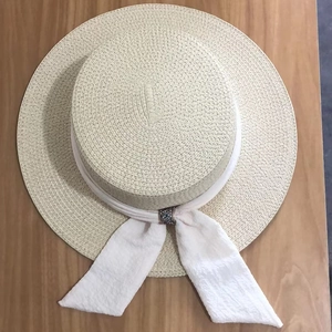 Close-up of beige straw boater hat with white chiffon ribbon and crystal buckle detail