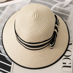 Close-up of beige straw sun hat with black and white striped ribbon and bow detail