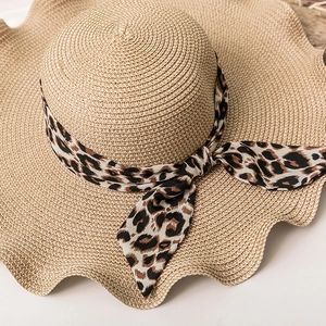Detailed close-up of straw sun hat with leopard print ribbon and wavy brim edge